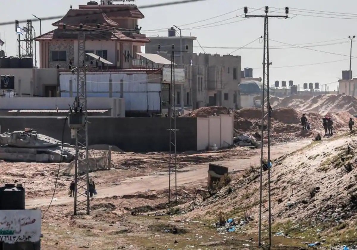 Mujeres palestinas desaparecidas cargando sus pertenencias pasan junto a las fuerzas israelíes en la zona de la ciudad de Hamad